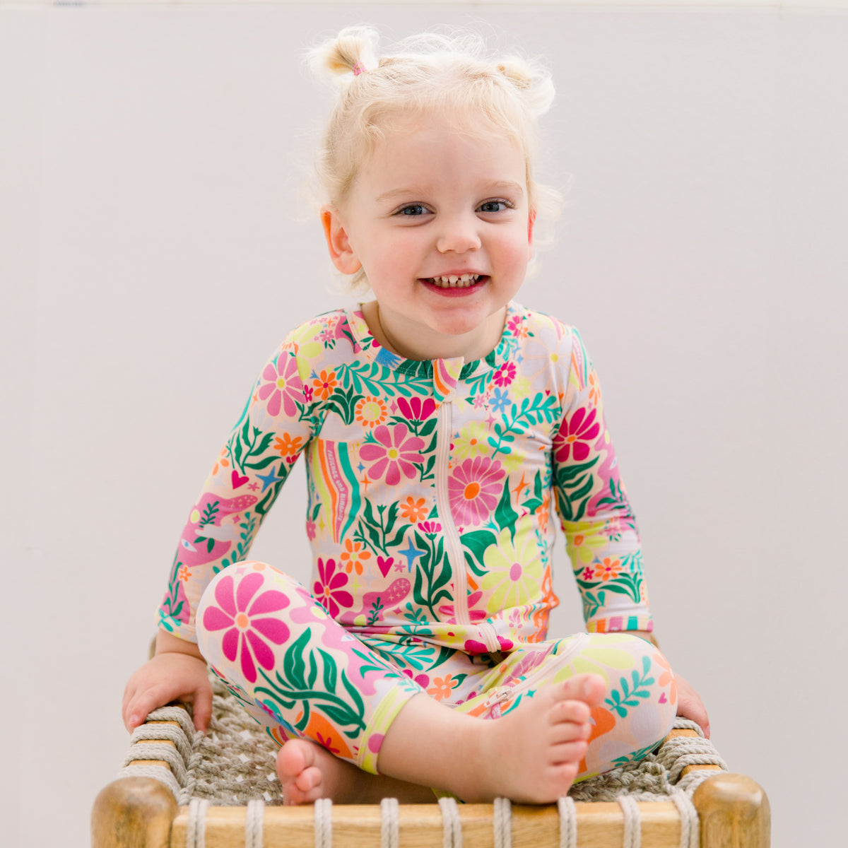 Baby girl wearing retro pink yellow and orange daisy rainbow bamboo pajamas from Rainbow Daisy Babe collection
